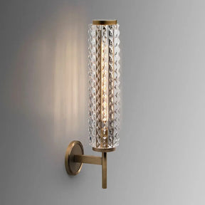 The Crystal & Copper Contemporary Wall Sconce by Morsale.com showcases a modern design with a cylindrical, textured glass shade elegantly mounted on a sleek brass arm and base. This LED wall light emits a warm, inviting glow, adding an elegant and sophisticated ambiance to any space when placed against a plain gray background.