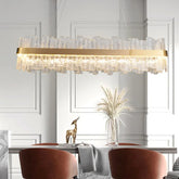 A modern dining room features the Ariano Frosted Glass Dining Room Chandelier by Morsale.com, boasting a gold electroplated finish and LED light source, hanging over a rectangular table. The table is adorned with a delicate wheat arrangement in a vase and a small deer sculpture, surrounded by red upholstered chairs.