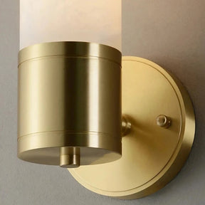 Introducing the Moonshade Natural Marble Sconce Light from Morsale.com, a wall-mounted cylindrical sconce featuring a frosted glass shade and a brushed brass finish. Its base is a circular brass-colored plate adorned with a small decorative knob next to the main fixture, perfectly complementing natural marble sconces when mounted on a neutral-colored wall.