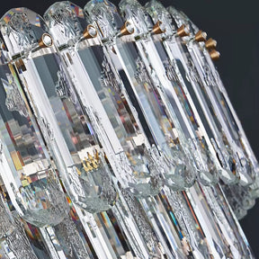 A close-up of the elegant Gio Crystal Chandelier by Morsale showcases intricate designs, featuring elongated crystals arranged in a row. Enhanced by LED bulbs, this chandelier reflects light to create a sparkling effect against a dark background, adding a touch of modern style.