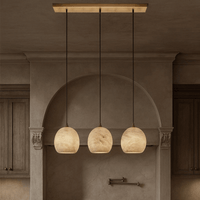 The Auris 3-Light Linear Marble Chandelier by Morsale.com features three globe pendants on adjustable cords, suspended in a row from a rectangular mount, adding ambient light to a neutral kitchen with wooden cabinets.