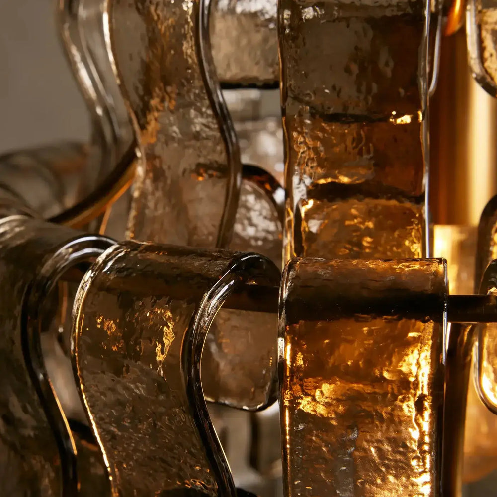 
                  
                    The Riviera Pendant by Morsale features wavy, hand-blown glass panels with warm light shining through, highlighting their curved shapes and glossy surfaces—ideal for modern lighting design.
                  
                