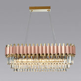 The Gio 39" Rose Gold Dining Room Chandelier by Morsale.com, a luxurious rectangular fixture, features a gold and rose gold frame with multiple tiers of hanging glass prisms. Suspended by two stainless steel cables from a gold ceiling mount, it emits a warm, elegant glow against a plain gray background. The chandelier includes dimmable LED lights.