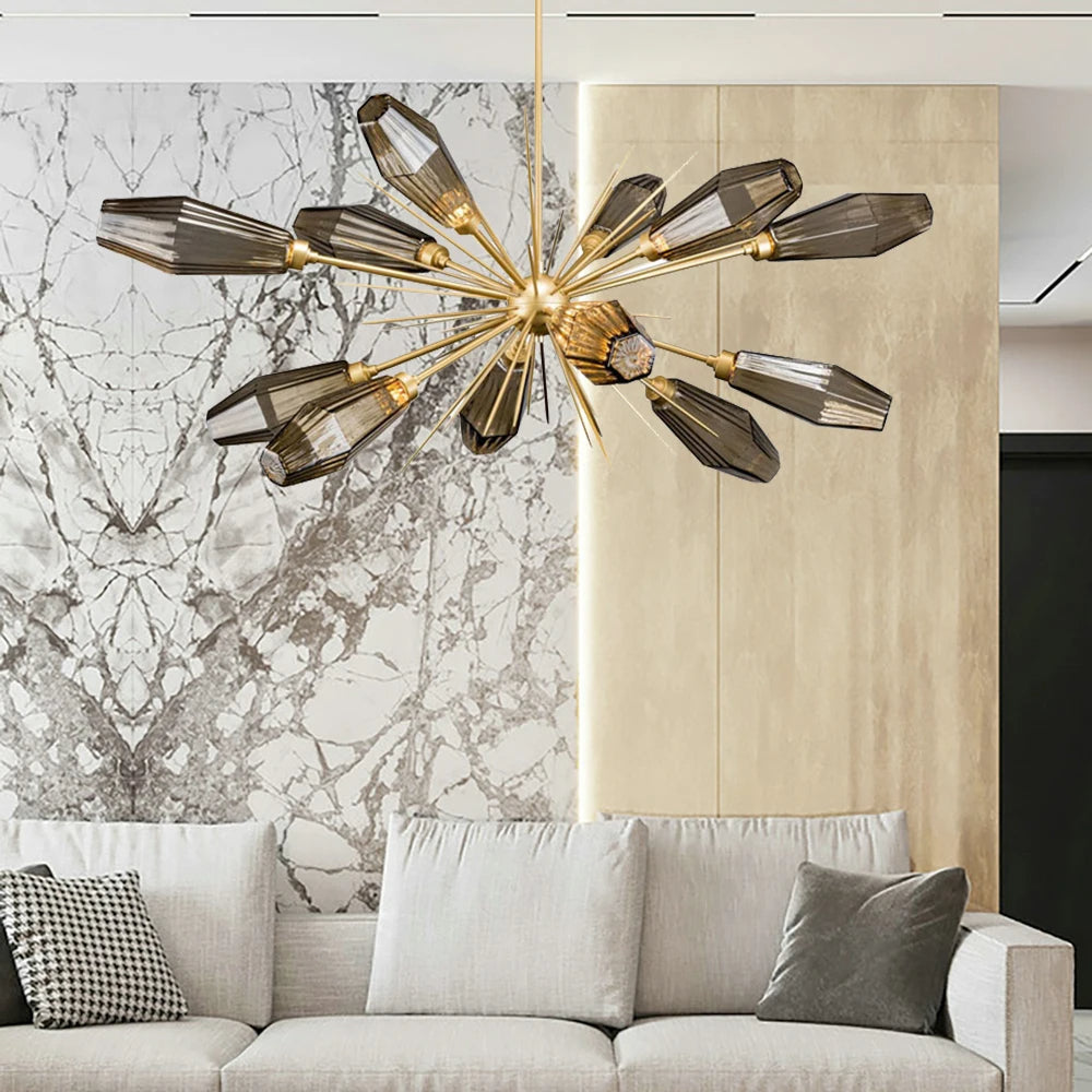 Modern living room with a white and beige color scheme featuring a large, gray sofa adorned with monochromatic throw pillows. Above the sofa hangs a striking Morelli Sputnik Chandelier by Morsale.com with multiple smokey-gray glass shades, and behind is an ornate marble accent wall, enhancing the modern elegance.