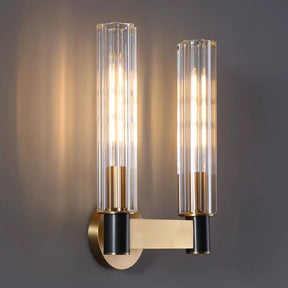 The Palermo 2-Head Retro Brass Wall Sconce by Morsale is a luxurious lighting fixture, featuring a contemporary design with two vertical cylindrical glass shades. Its warm light and retro brass base, complemented by a black horizontal bar, create an elegant contrast against a dark gray background.