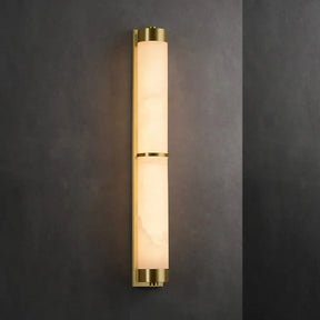 A 23" Natural Marble & Brass Wall Light by Morsale with a sleek, vertical design featuring two connected cylindrical frosted glass shades with brass accents mounted on a dark wall. The ambient, energy-efficient LED light glows warmly, enhancing the minimalist, contemporary style.