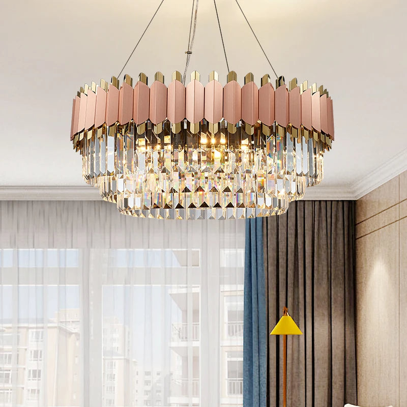 A Gio Rose Gold Modern Chandelier from Morsale.com with a geometric design featuring gold and pink rectangular elements hangs from the ceiling in a well-lit room. Handcrafted crystals add elegance, while sheer curtains, a gray sofa, and a yellow floor lamp complete the look.