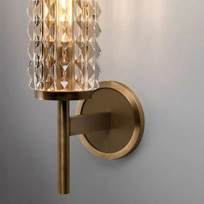 The Crystal & Copper Contemporary Wall Sconce by Morsale.com features a cylindrical, faceted glass shade paired with a brass-colored metal base. When illuminated, it casts a warm glow on the surrounding wall, making it an ideal addition to any contemporary decor.