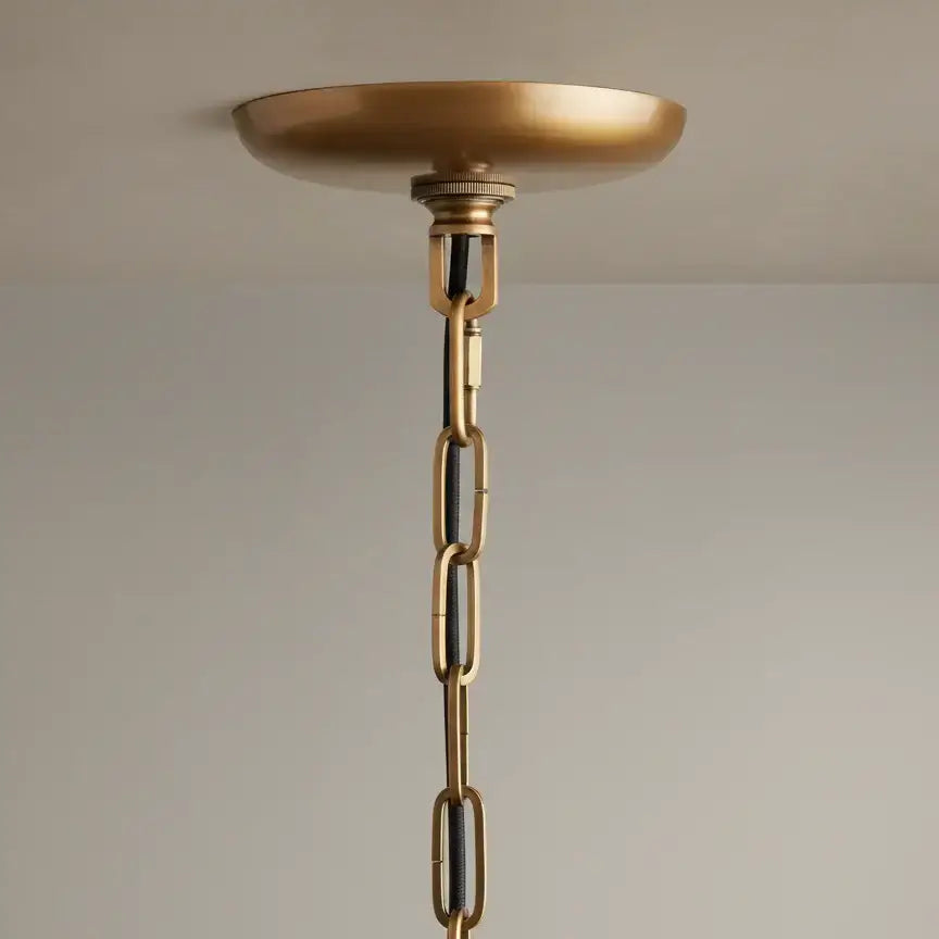 
                  
                    A close-up of Morsale's Riviera Pendant shows its brass ceiling canopy with chain and cord, set against a beige wall—ideal for hanging this modern minimalist fixture.
                  
                