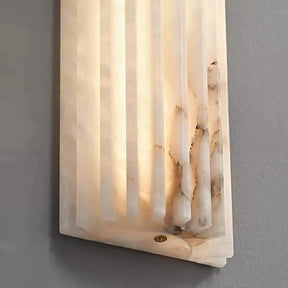 Close-up of the Morsale Natural Marble LED Wall Sconce featuring a translucent, ribbed beige cover with dark veining. It casts a soft, warm glow on any gray wall and showcases a geometric, layered design with subtle texture, perfect for modern spaces in need of stylish lighting solutions.
