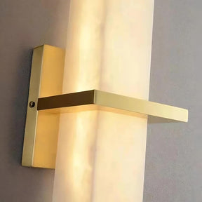 A minimalist wall light fixture with a warm glow, featuring a rectangular, horizontal, brushed gold metal arm intersecting a vertical frosted cylindrical light diffuser. The Morsale.com Natural Marble Indoor Sconce is mounted on a square base attached to a light-colored wall, perfect for LED indoor lighting.