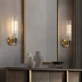 A modern interior features a wooden console table with three decorative items: two white vases and a dark bowl. Above the table, a large rectangular mirror is flanked by two Morsale Palermo Retro Brass Wall Sconce lights emitting warm light, each boasting a brass finish and clear glass shade.