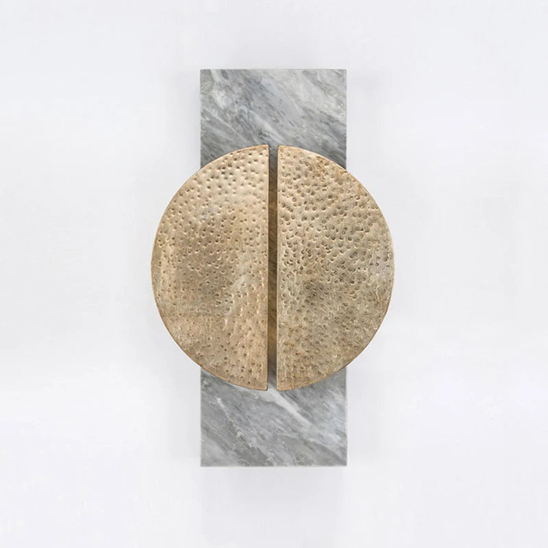 A modern wall sculpture featuring a vertical rectangular slab of Natural Spanish marble with a large circular bronze element divided into two semicircles with a textured surface, placed at the center, evocative of the Medieval Marble Wall Light Sconce by Bigman.