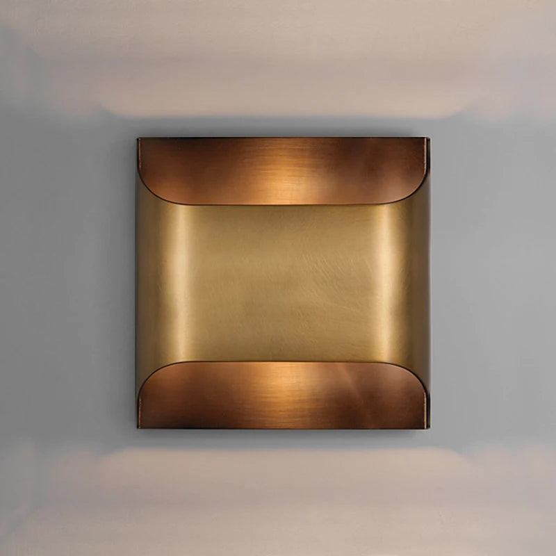 The Rame Modern Copper Wall Lights by Morsale offer a minimalist design, showcasing a square sconce with a curved, polished copper finish. Its warm, golden tone beautifully contrasts against a neutral gray background, making it perfect for enhancing your home decor lighting with elegance.