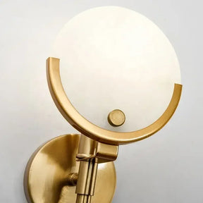 The Moonshade Marble Wall Light Sconce by Morsale.com showcases a minimalist brass wall light fixture with a circular frosted glass shade and a round brass base. Its warm, golden finish and distinctive marble texture add an effortlessly modern touch to any space.