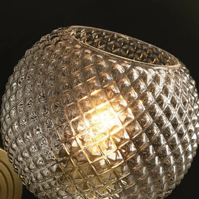 A close-up of a glowing light bulb inside a spherical, textured glass globe. The glass lampshade has a diamond pattern, adding a decorative effect to the lighting. The background is dark, highlighting the Morsale Palermo Wall Sconce Light's warm glow and intricate design.