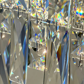 A close-up image of interlocking, clear, rectangular crystals reflecting light in various colors is reminiscent of the Bacci Crystal Modern Dining Room Light Fixture 47" by Morsale.com. The geometric arrangement creates a luxurious pattern with multicolored light scattering across the surfaces, evoking the elegance of a modern dining room light.