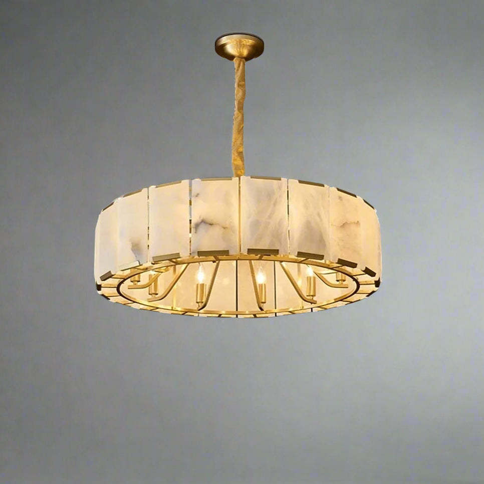 A modern Natural Marble Ceiling Chandelier by Morsale.com with a cylindrical, semi-translucent white and gold frame hangs from the ceiling. Below, the room features dark walls, framed geometric artwork, a large window with sheer white curtains, and a potted plant in the corner. The G9 LED bulbs add an elegant glow to the space.