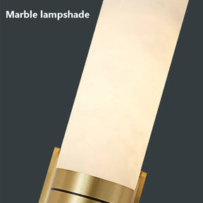 A Natural Marble Indoor Wall Sconce Light by Morsale.com is depicted, featuring a sleek, cylindrical design with a unique texture. The wall sconce light is positioned vertically, emanating a soft, warm light from its brass light source. The base is metallic with a golden hue. The text "Natural Marble Indoor Wall Sconce Light" by Morsale.com is in the top left corner.