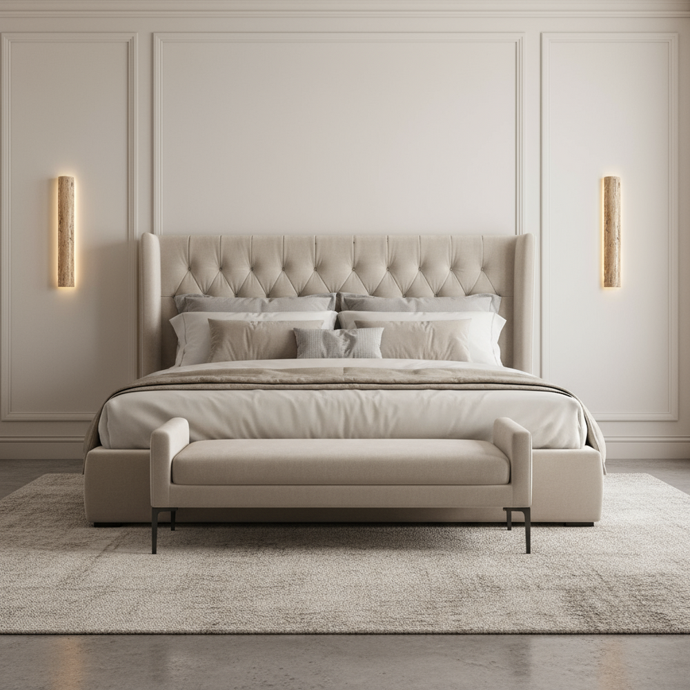 A modern bedroom featuring a beige tufted bed, matching bench, neutral bedding, textured rug, and two Morsale Solterra Travertine Sconces with integrated LED on a light-paneled wall.
