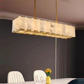 A modern rectangular chandelier from Morsale.com, known as the Natural Marble Ceiling Chandelier, hangs over a long dining table. The table is set with two glasses and a vase containing yellow tulips. The room decor features a dark wall and light, cushioned chairs, perfectly complemented by the elegant brass light fixture.