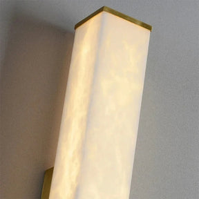 A close-up view of the Natural Marble Indoor Wall Sconce Light by Morsale.com. The frosted, slightly translucent surface glows with soft white indoor LED lighting. It features brass light fixture trim at the top and bottom edges, mounted on a neutral-colored wall.