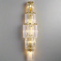 The Gio Crystal Wall Sconce by Morsale.com features tiered, gold-framed clear crystal rods in a symmetrical pattern. Dimmable LED bulbs emit a warm glow through the glass, enhancing any neutral wall with elegance.