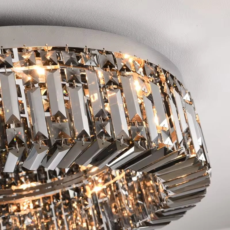 A close-up of the Specchio Smoke Grey Crystal Ceiling Light from Morsale.com showcases multiple angular crystal prisms that create a sparkling, reflective effect. Illuminated by E14 LED bulbs, the fixture emits a warm glow, enhancing the intricate design and the smoke grey crystal's clarity and brilliance.