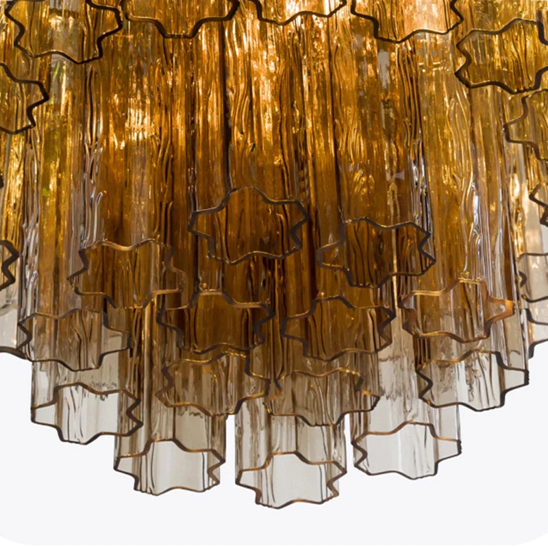 
                  
                    Close-up of the Burney Modern Chandelier by Morsale, featuring layered amber glass tubes with wavy, star-shaped edges for a cascading decorative effect and warm glow.
                  
                