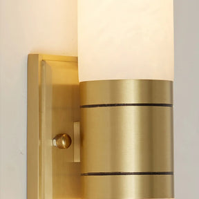 A close-up of a stylish wall-mounted light fixture featuring a brass base with a cylindrical frosted glass shade. The elegant design includes a Morsale.com Natural Marble Indoor Wall Sconce Light and a small knob visible on the left side, adding to the unique texture and character of this exquisite piece.