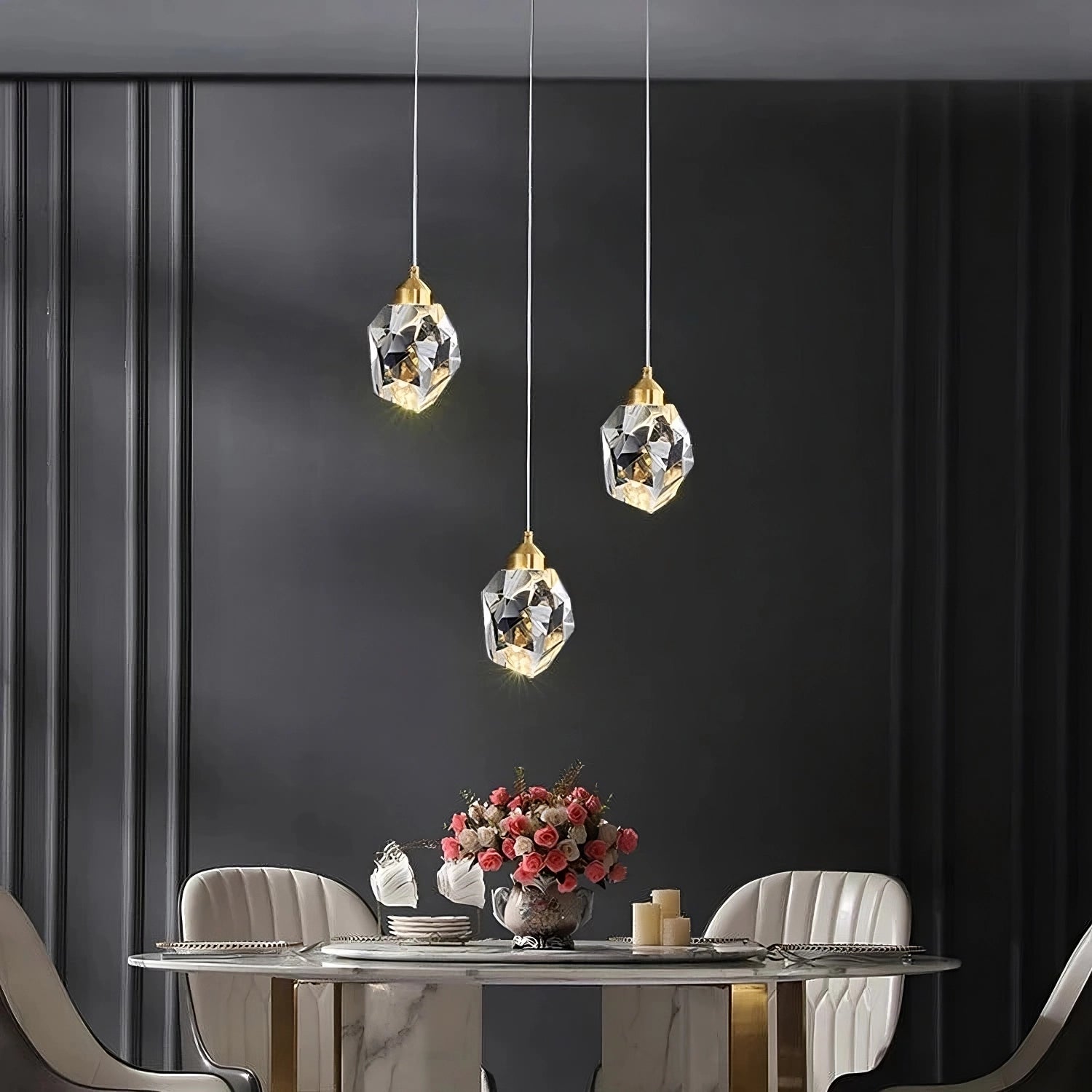 A sophisticated dining area showcases a round marble table adorned with a floral centerpiece and surrounded by elegant chairs. Hanging above are three Diamante Crystal Pendant Lights by Morsale, which enhance the modern style ambiance set against a dark, textured wall.