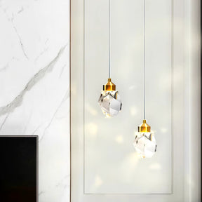 Two Diamante Crystal Pendant Lights by Morsale, featuring modern design with gold accents, hang elegantly against a white panel wall. They create shimmering reflections on the surface, enhancing the soft atmosphere. A touch of a marble-patterned wall is visible to the left.