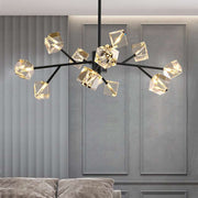 A contemporary Diamante Crystal Ceiling Light Fixture from Morsale.com, featuring black branches and geometric, gold-toned light fixtures, is elegantly suspended from the ceiling. It hangs gracefully above a grey sofa set against a textured wall with vertical lines and panel detailing.