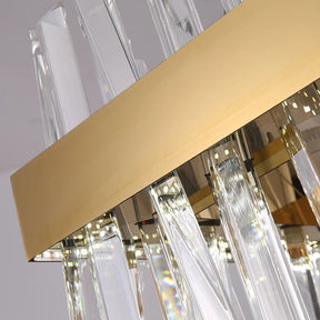 A close-up view of the Calvi Crystal Dining Room Light Fixture by Morsale.com showcases its modern chandelier design with a circular gold metal frame, adorned with vertical rectangular handmade crystals extending upwards. The crystals reflect and refract light, creating a dazzling effect that makes this stunning piece an exquisite addition to dining room lighting. The background is a plain, light-colored surface.