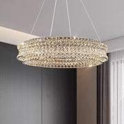 The Bacci Modern Crystal Chandelier by Morsale, with three circular, crystal-studded rings and energy-efficient LED bulbs, casts a soft, warm glow in a contemporary room with gray walls and white curtains by the window.