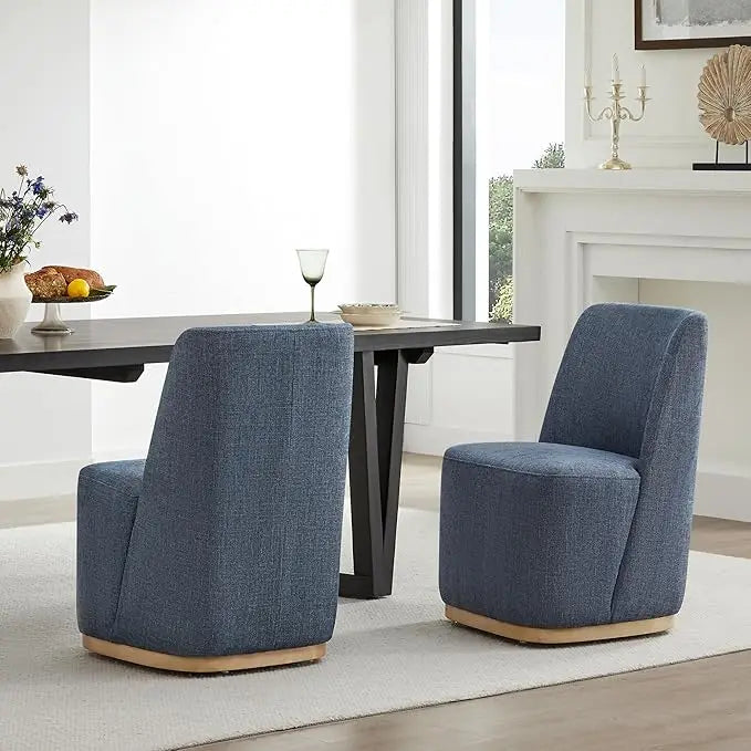 Two Morsale Boucle Dining Chairs With Casters sit around a dark rectangular table with a wine glass. Large windows, a white mantel with decor, and a light rug brighten the room.