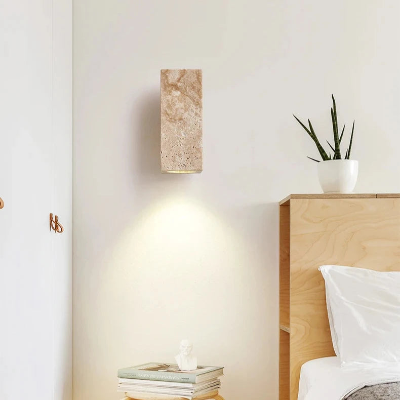 The Natural Travertine Wall Lights from Morsale.com feature a wall-mounted light fixture with a rectangular, stone-like cover and a wooden mounting base. The LED wall lamp directs light downward, casting a soft glow on the gray wall below, embodying Japan-style lighting aesthetics.