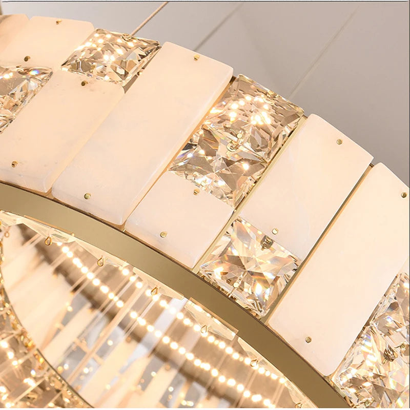 
                  
                    Close-up of the Morsale Edes Crystal & Marble Chandelier, featuring alternating rectangular crystals and white marble-like panels that emit warm light with sparkling reflections.
                  
                