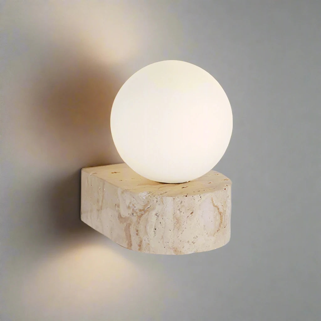 The Modern LED Travertine Wall Sconce from Morsale.com features a travertine base with natural beige and light brown patterns, topped with a large, smooth frosted globe light. Equipped with LED bulbs, the globe emits a soft, warm glow that casts gentle light on the wall.