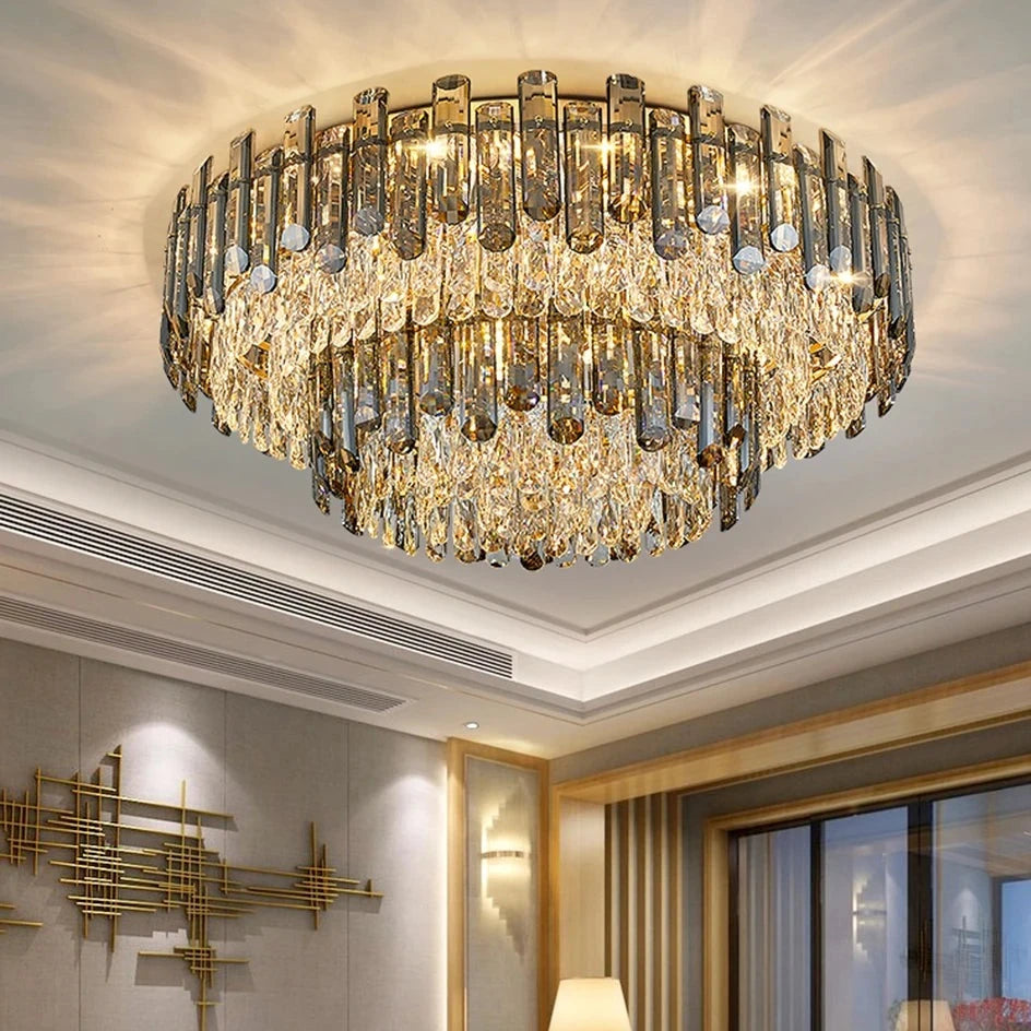 A luxurious living room features a grand Venice 2-Tier Crystal Chandelier by Morsale.com with cascading crystal-like elements hanging from the ceiling. The room is decorated with modern furniture, including a sectional sofa with patterned cushions, a coffee table, and ambient lighting for sophisticated décor.