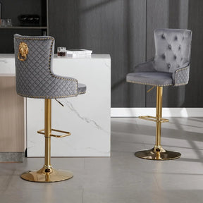 Morsale's Diamond Lattice Wingback Counter Stools elegantly accompany a marble-topped counter with quilted gray upholstery and gold bases. One stool has a lion emblem, enhancing the minimalist room's modern charm, featuring dark walls and a light floor.