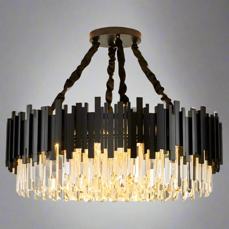 The Gio Modern Chandelier by Morsale features a contemporary circular design with staggered black and clear glass elements. It has a crystal shade suspended from a round ceiling mount with four twisted black cables, creating a warm glow.