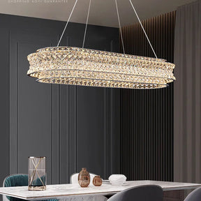 A modern dining room features a Bacci Modern Crystal Chandelier by Morsale with LED bulbs hanging over a marble table, adorned with decorations and surrounded by elegant chairs. Dark paneled walls and long curtains enhance the sophisticated ambiance.