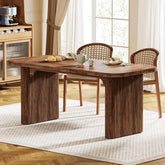 The York 63" Dining Table by Morsale, featuring a ribbed design and paired with two matching chairs on a light-textured rug, embodies modern style. A teapot, cups, and pastries adorn the tabletop. Large windows with sheer and brown drapes enhance the inviting atmosphere.