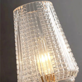 A detailed view of the Morsale Palermo Copper & Glass Contemporary Wall Sconce shows its decorative glass lamp shade with a textured pattern, illuminated by an energy-efficient LED bulb inside. The glass design includes vertical ridges and square patterns, casting a warm copper glow against a gray backdrop.