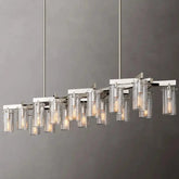 A modern rectangular chandelier with a brushed nickel frame hangs from the ceiling. Featuring multiple cylindrical glass shades with a textured finish, this Leroi Chrome Dining Room Chandelier by Morsale holds individual lights that emit a warm glow, creating an elegant and sophisticated lighting fixture.