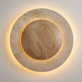 The Natural Travertine LED Decor Wall Light by Morsale.com is a modern LED wall lamp with a circular design, featuring a wooden central circle surrounded by a stone-like ring, both illuminated with a soft, warm glow. Blending Art Deco style and daily lighting needs, this piece creates a serene and ambient atmosphere.