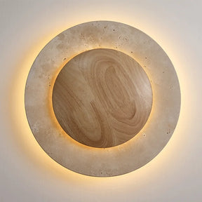 The Natural Travertine LED Decor Wall Light by Morsale.com is a modern LED wall lamp with a circular design, featuring a wooden central circle surrounded by a stone-like ring, both illuminated with a soft, warm glow. Blending Art Deco style and daily lighting needs, this piece creates a serene and ambient atmosphere.