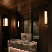 Luxurious bathroom featuring a sleek, dark marble sink and countertop, surrounded by rich wood paneling. The Alton Marble Wall Lamps by Morsale alongside the large mirror and modern fixtures enhance the warm, elegant ambiance with a touch of modern style.