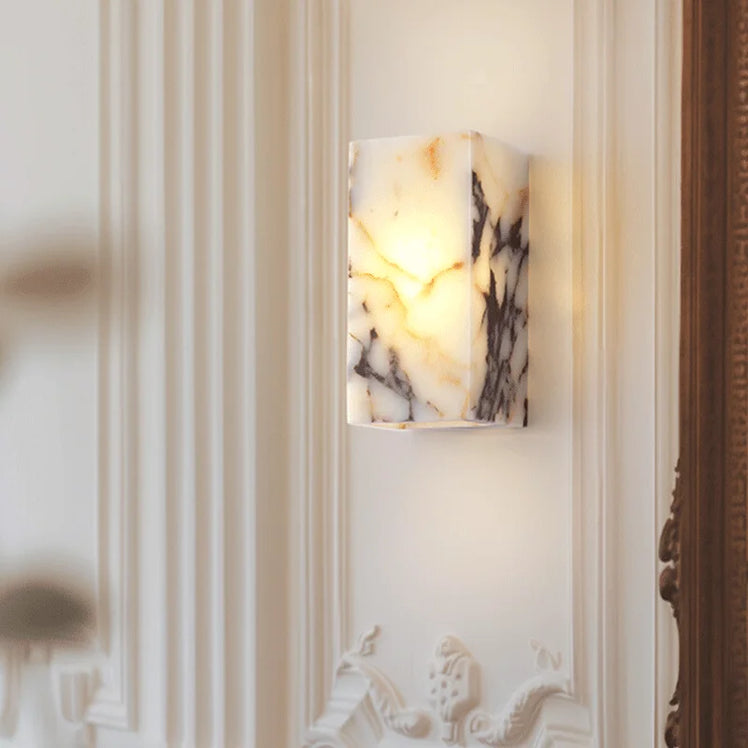 The Moonshade Natural Stone Wall Lamp by Morsale is an elegant wall-mounted sconce with LED lighting, gently illuminating the intricately designed white wall with decorative molding. Its rectangular shape and natural marble pattern bring timeless Art Deco sophistication.